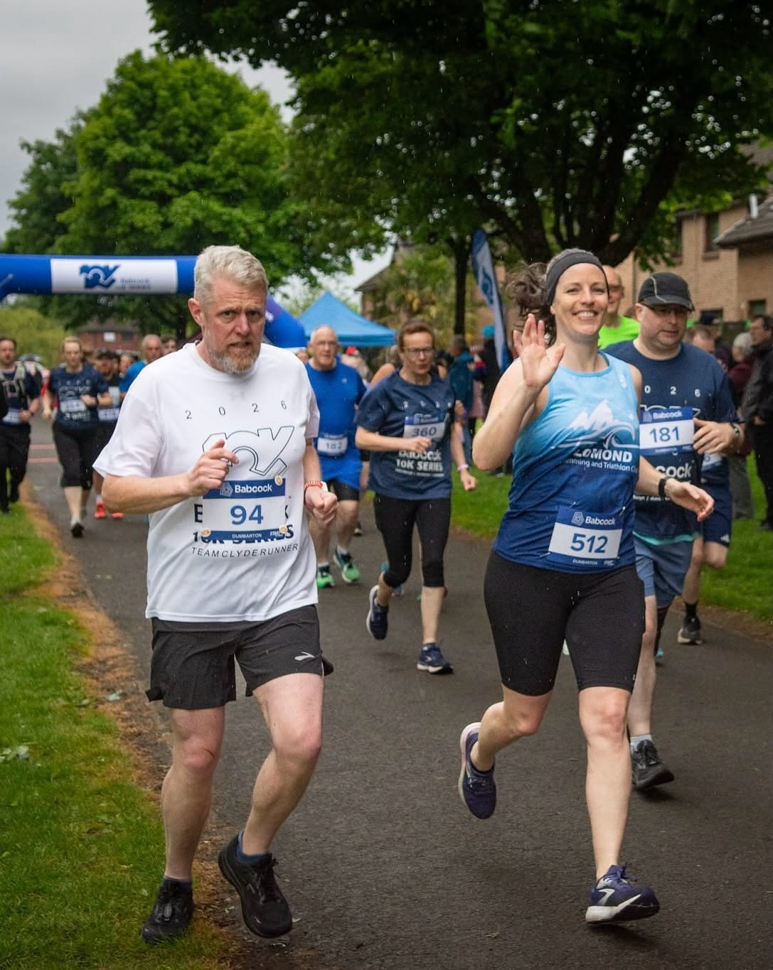 A Lomond runner waving during a busy road race
