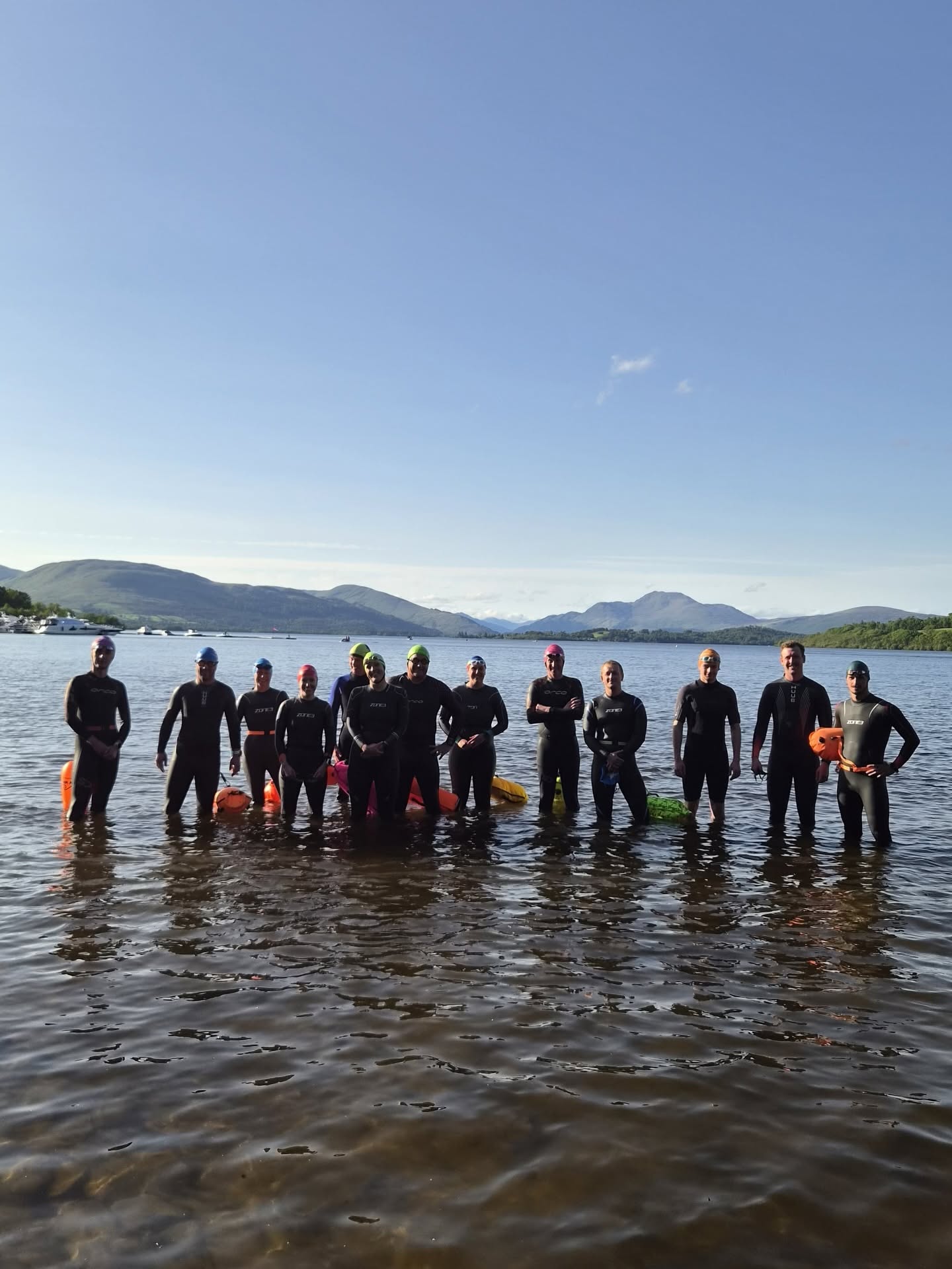A group of Lomond swimmers standing in Loch Lomond on a sunny evening